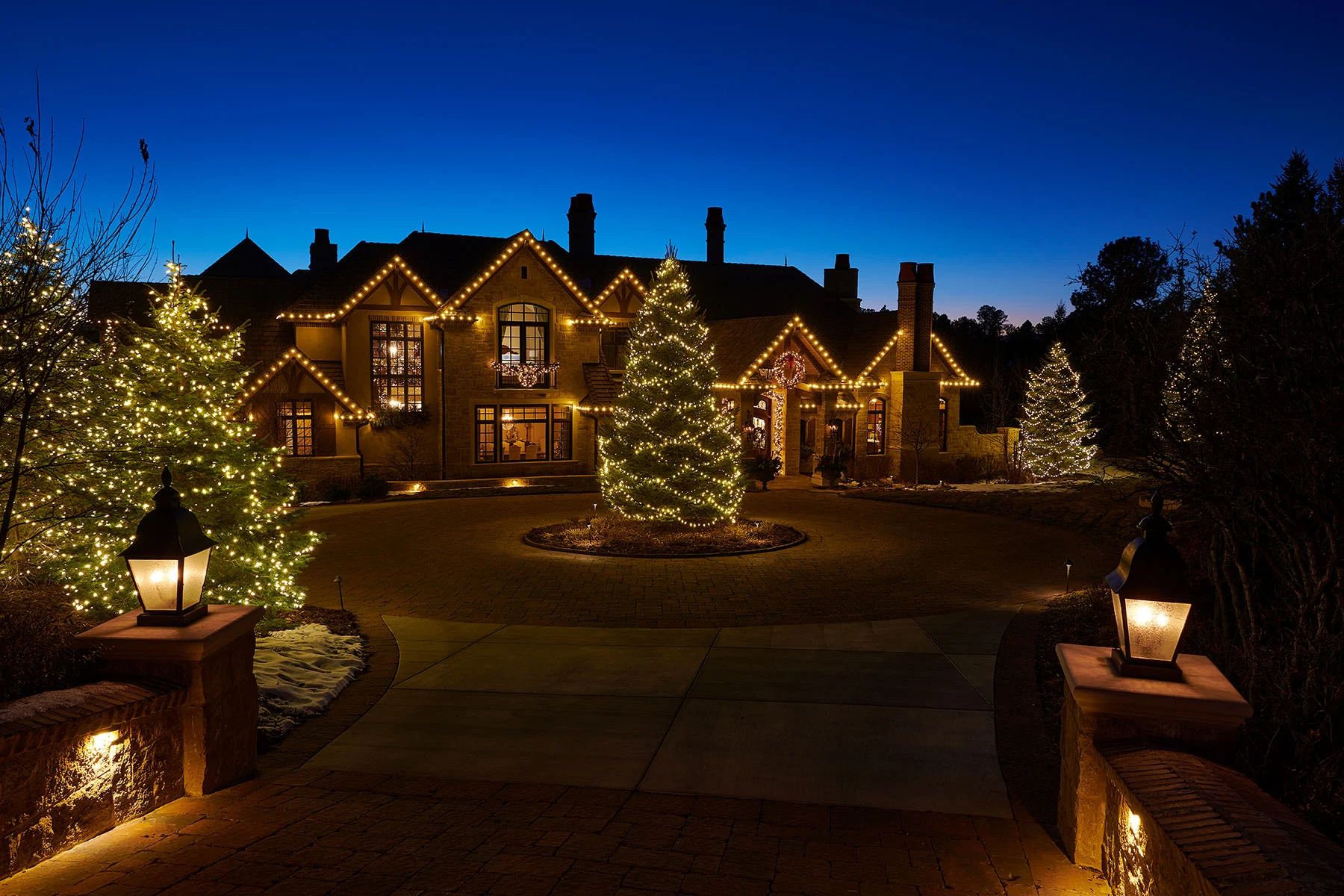 Luxury home with premium warm white Christmas lights on rooflines and trees.